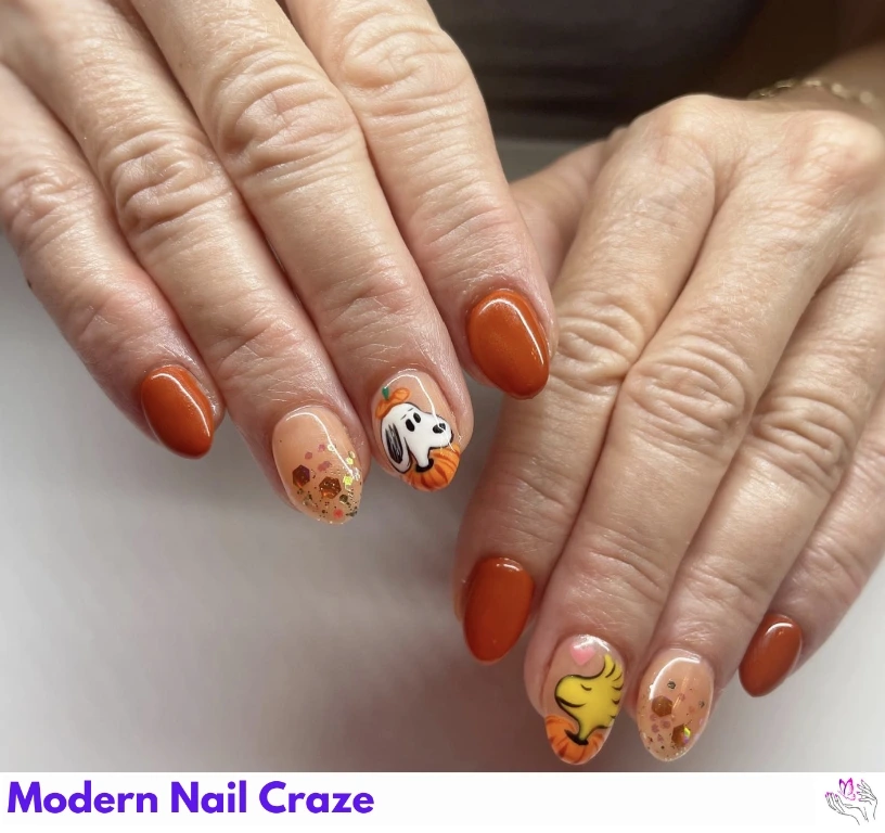 Snoopy and Woodstock cartoon nails with burnt orange and gold foil accents.